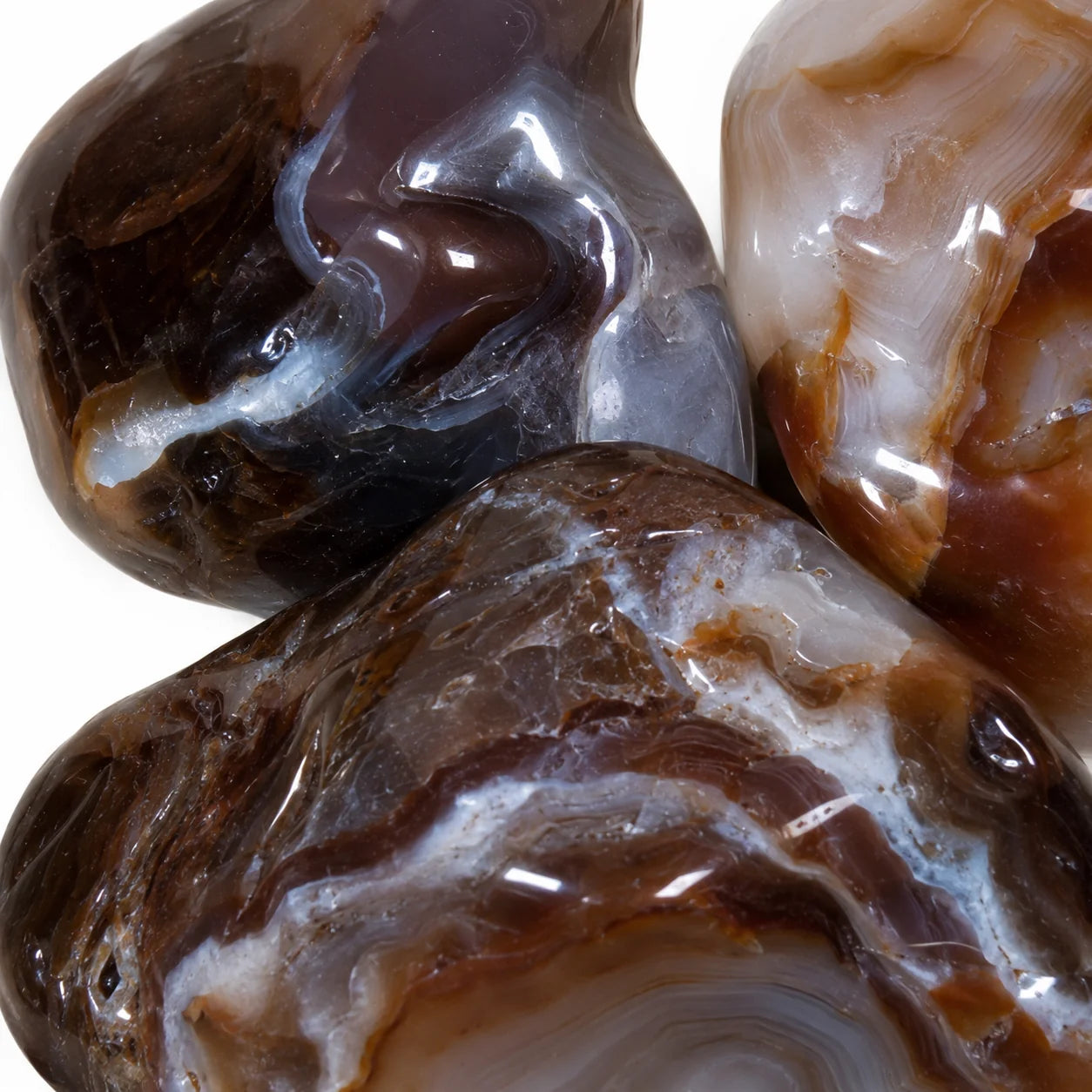 Gros plan sur trois agates de feu roulées du Mexique révélant leurs bandes naturelles, leurs teintes brun rouge, gris et blanc ainsi que leur surface polie brillante, photographie macro haute définition.