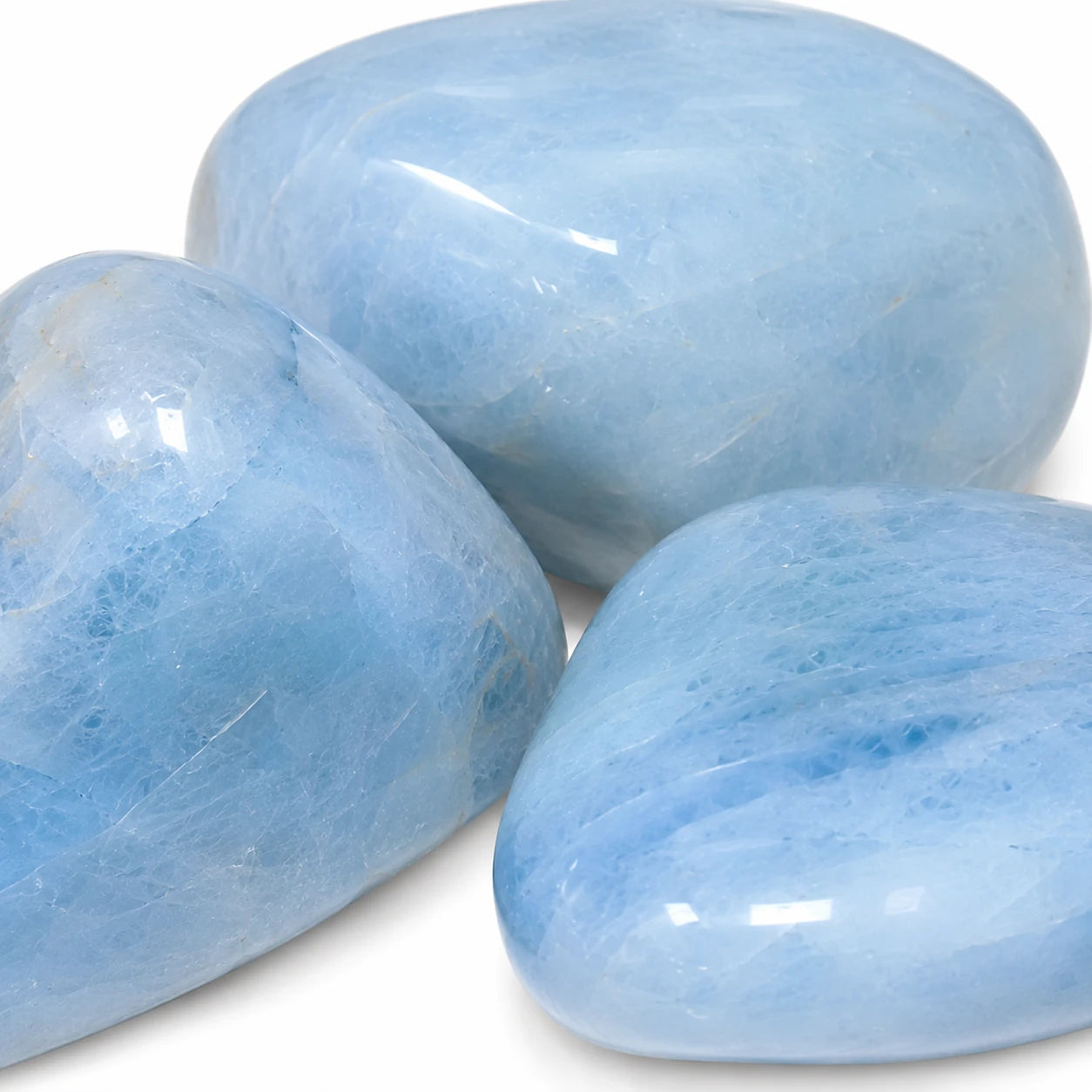 Gros plan sur trois pierres roulées d'Aigue-marine du Brésil, mettant en valeur leur couleur bleu ciel naturelle, leur transparence et leur surface polie.