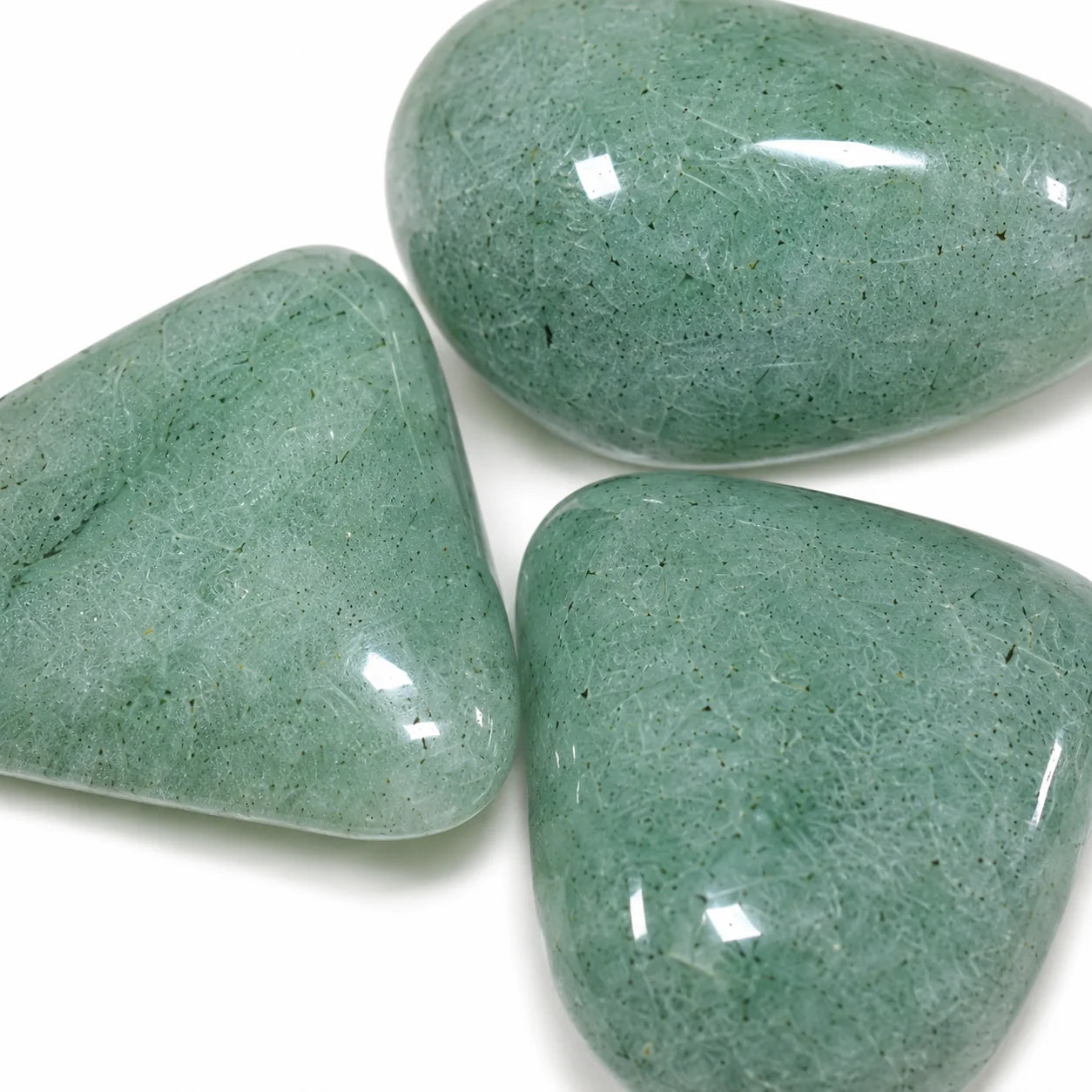 Gros plan de trois pierres naturelles aventurine verte roulée de Tanzanie, surface polie brillante révélant la texture minérale et les nuances vert tendre caractéristiques de cette pierre naturelle.