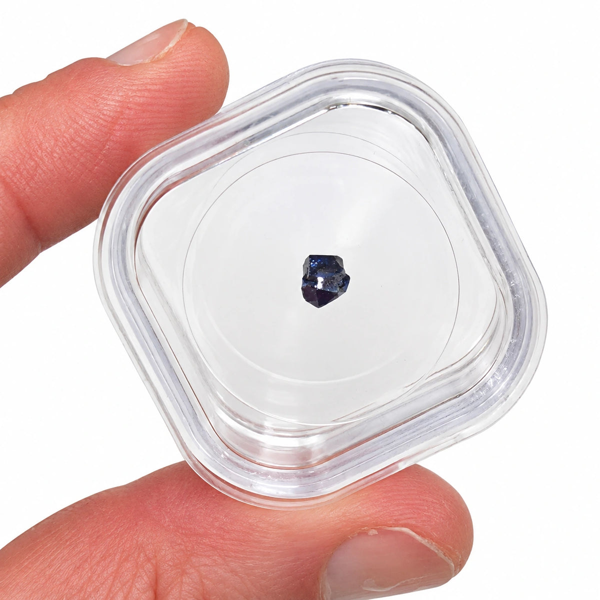 Petit cristal brut de boléite du Mexique, minéral bleu noir à l'éclat brillant, présenté dans une boîte transparente tenue entre les doigts.