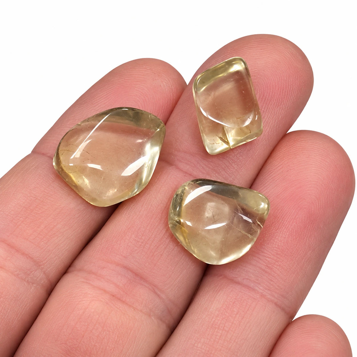 Trois petites pierres roulées naturelles Bytownite de Madagascar, aussi appelée labradorite dorée, présentées dans la main pour montrer leur taille