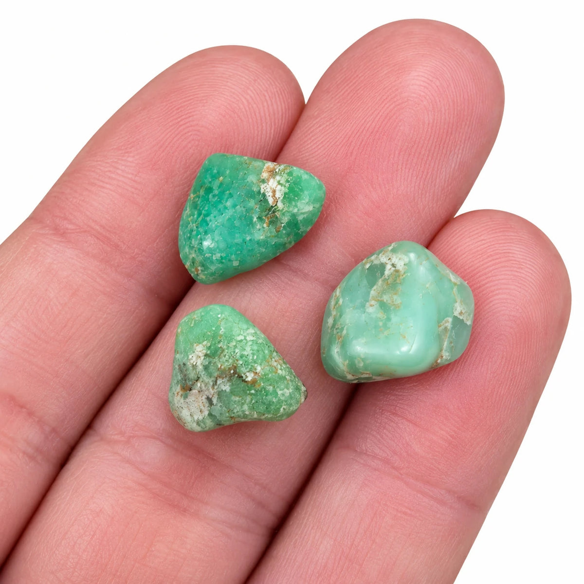 Chrysoprases roulées de très petite taille posées sur les doigts, montrant leurs nuances vertes et leurs inclusions blanchâtres