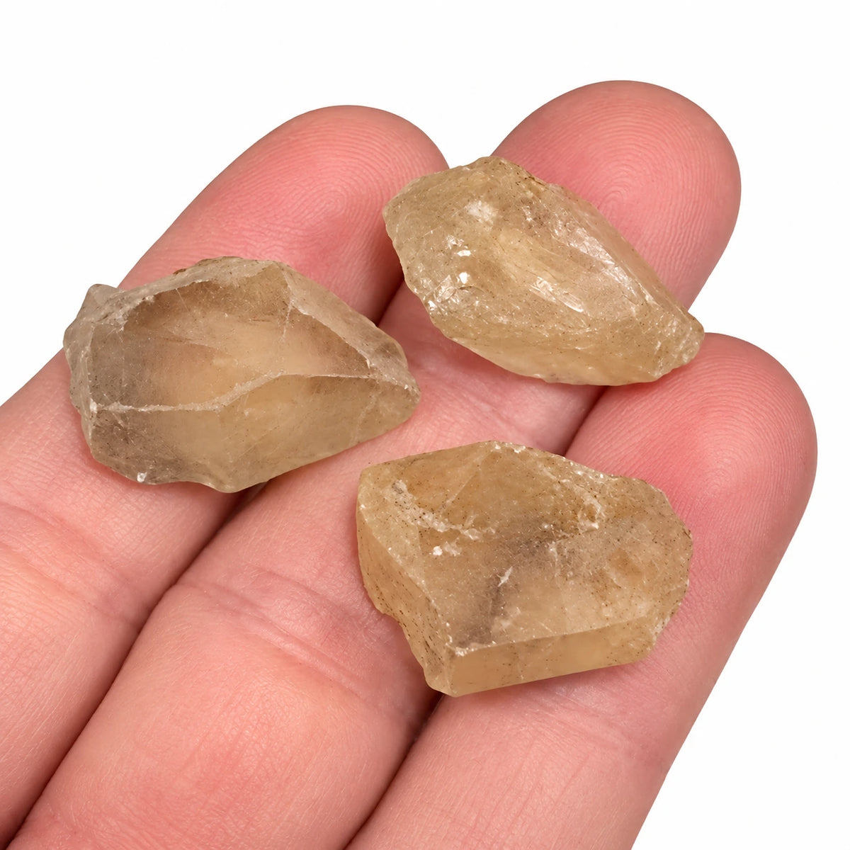 Trois petites pierres brutes citrine naturelle du Brésil posées dans la main, montrant leurs teintes jaune doré et leur aspect translucide