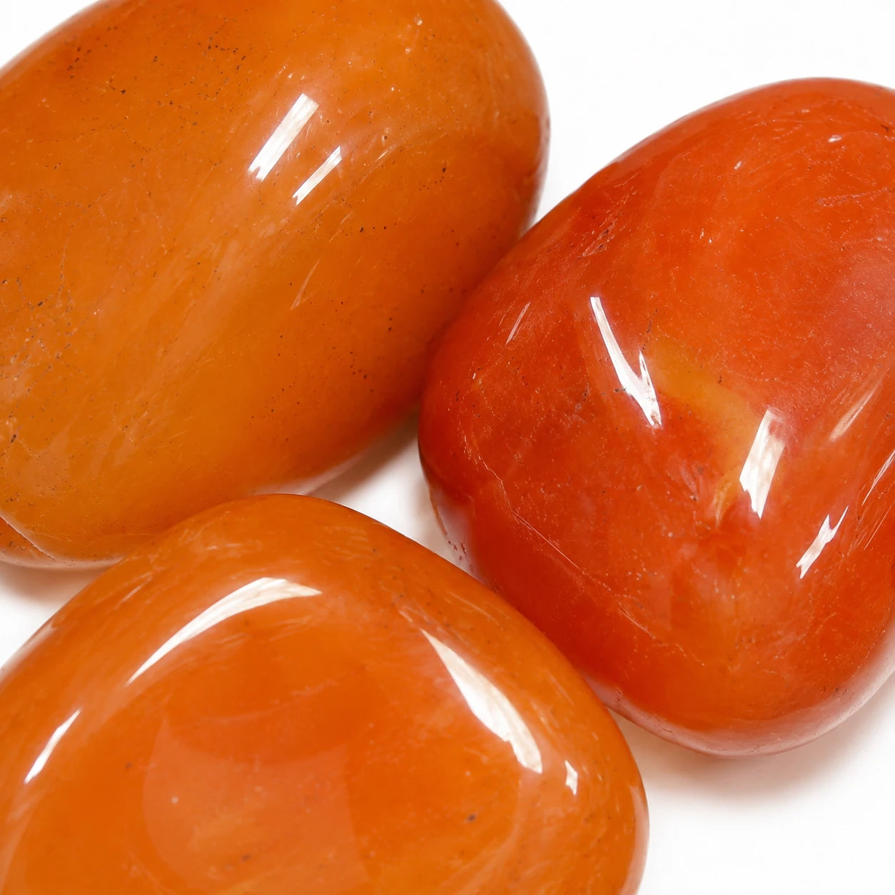 Pierre naturelle cornaline roulée du Botswana – gros plan sur trois pierres roulées polies révélant leur couleur orange translucide et leur éclat naturel.