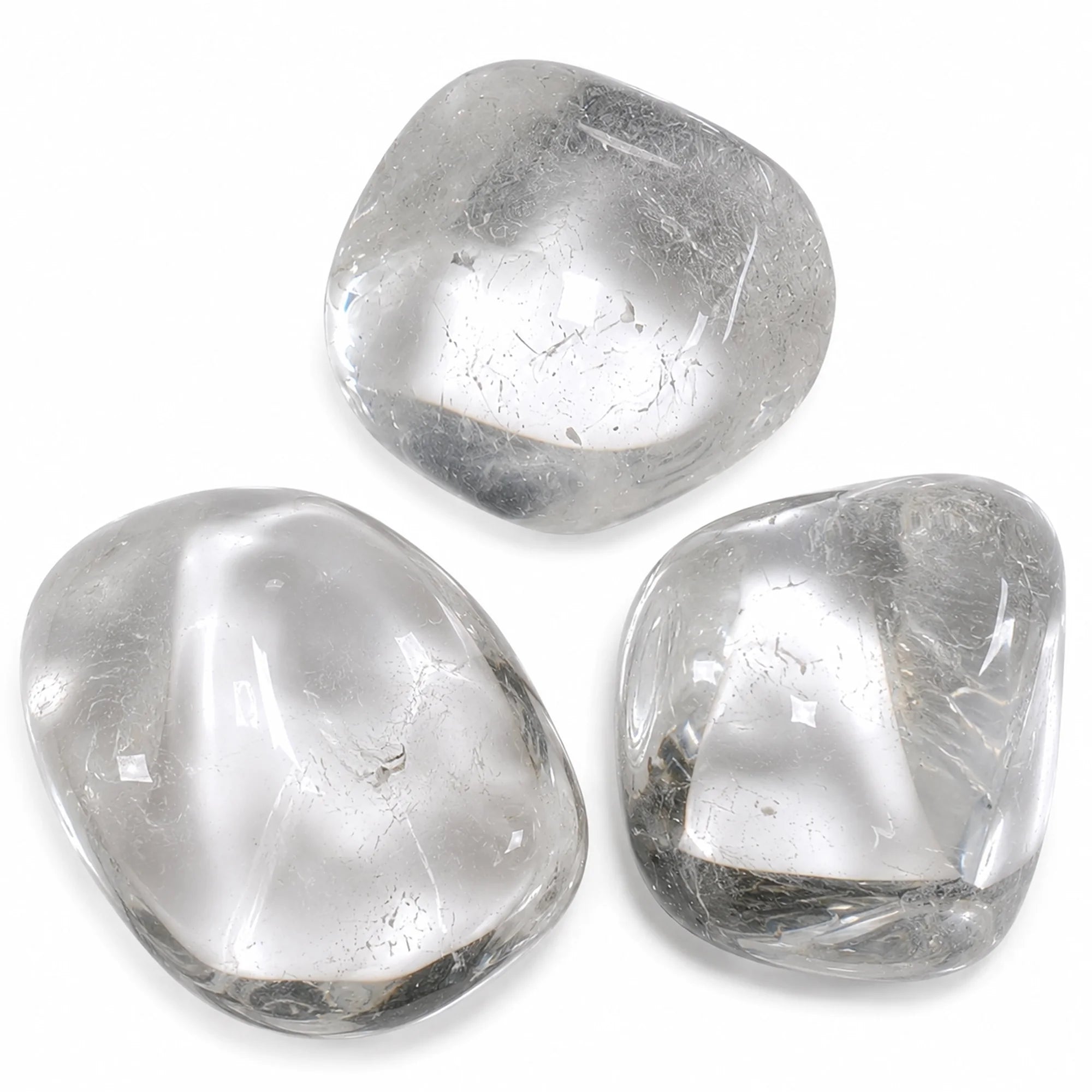 Pierre naturelle cristal de roche roulé du Brésil – gros plan sur trois pierres roulées en quartz transparent aux formes polies, sur fond blanc, révélant leur pureté et leurs inclusions naturelles.