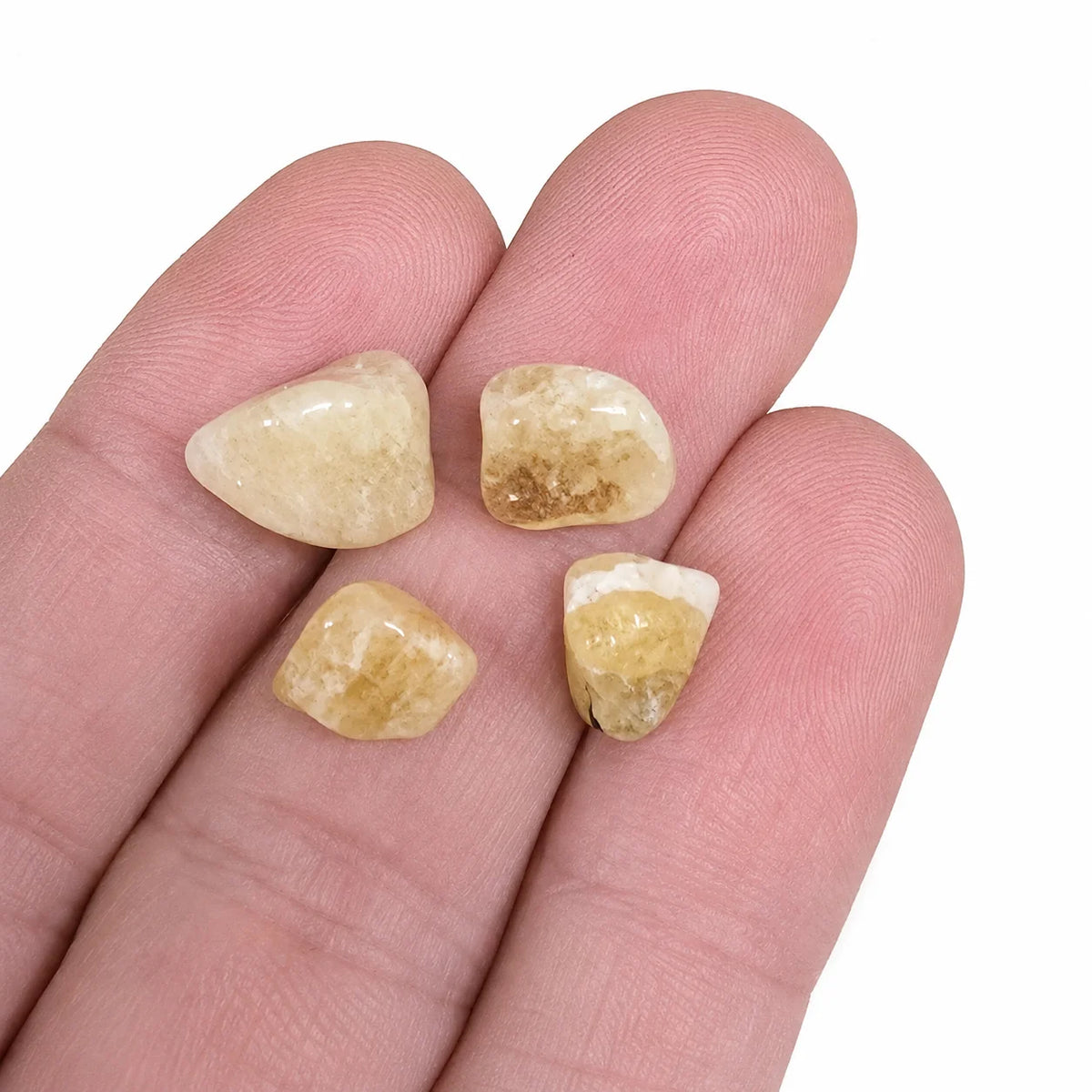 Quatre petites pierres naturelles héliodore roulées du Brésil tenues dans la main, pierres polies aux nuances jaune pâle et dorées