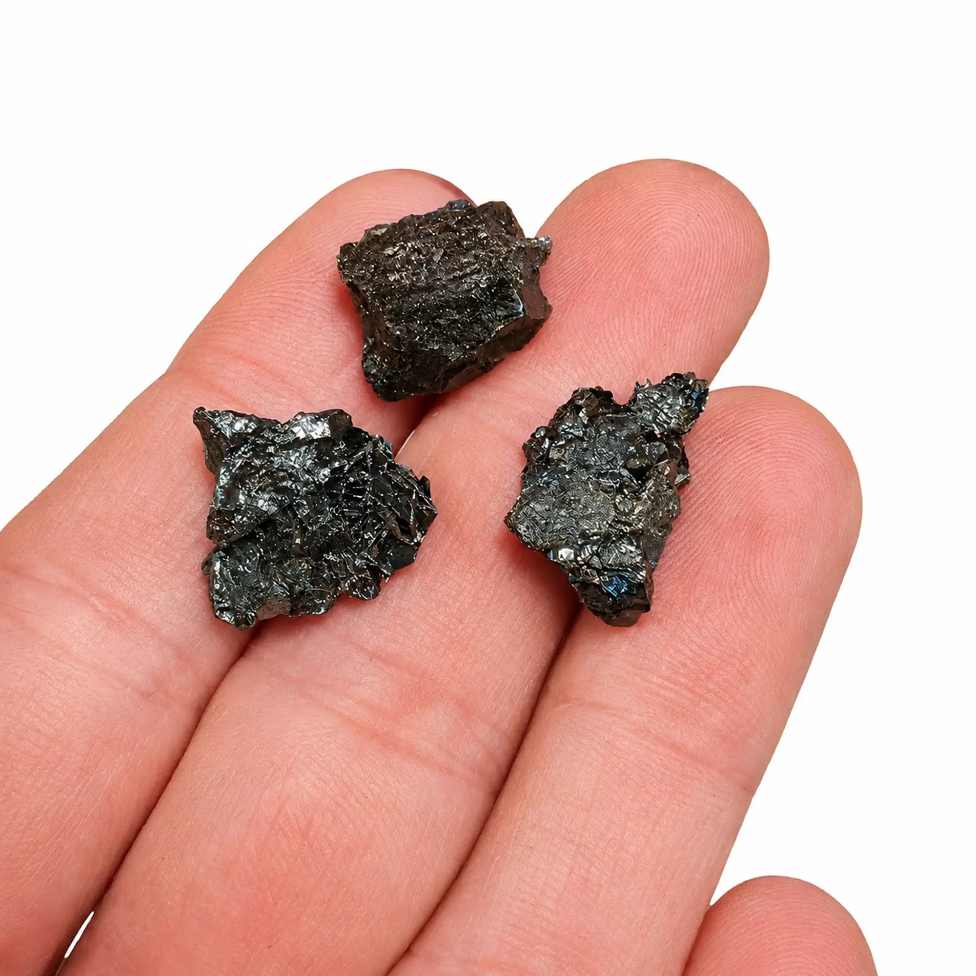 Trois petites pierres brutes d’hématite spécularite de l’île d’Elbe en Italie présentées dans la main, avec leurs reflets métalliques naturels