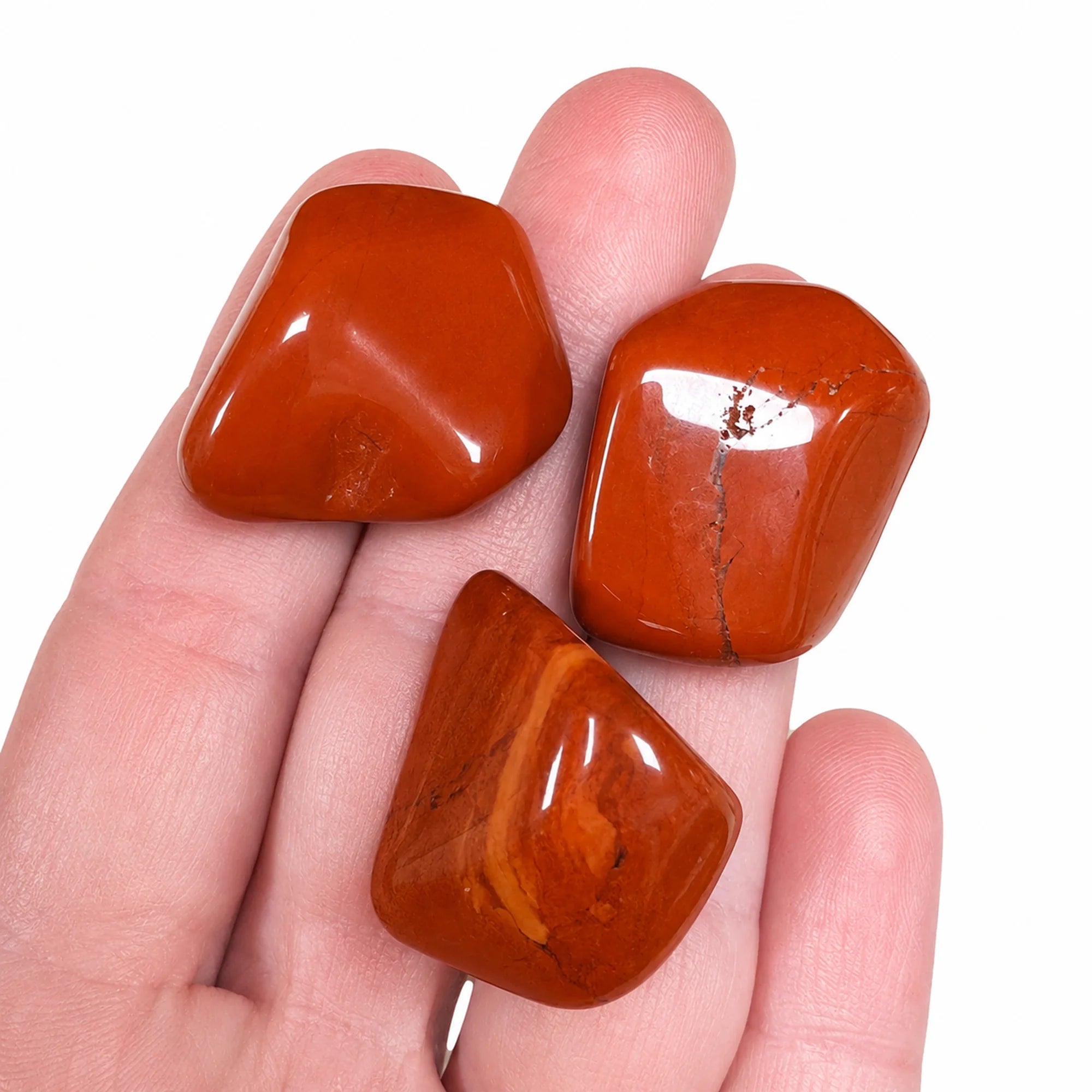 Pierre naturelle jaspe rouge roulé d'Afrique du Sud tenue dans une main, trois pierres polies rouge orangé