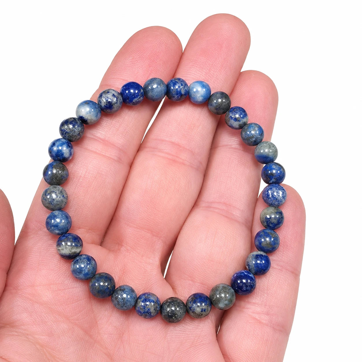 Bracelet en véritable lapis lazuli à perles rondes de 6 mm présenté dans une main pour illustrer sa taille réelle, pierre naturelle aux nuances de bleu profond et clair.