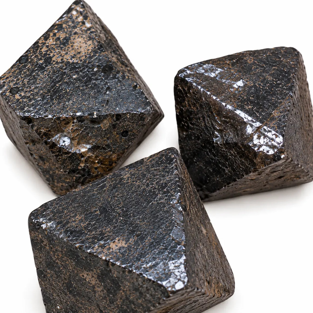 Gros plan de trois cristaux bruts de magnétite du Pérou, montrant leurs surfaces sombres, leur éclat métallique et leurs inclusions brunâtres.