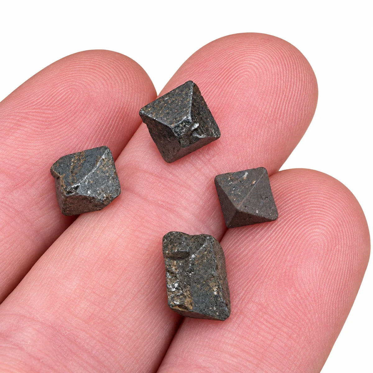 Petits cristaux de magnétite brute du Pérou présentés sur le bout des doigts, révélant leur forme géométrique, leurs reliefs naturels et leurs reflets gris métallisé.