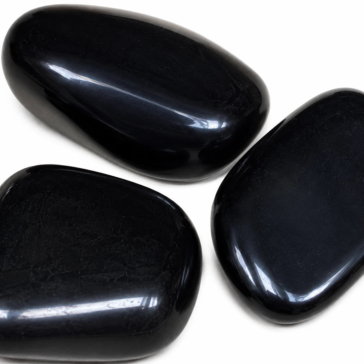 Gros plan sur trois pierres naturelles obsidienne noire roulée du Mexique, galets polis noirs brillants révélant leur surface lisse et leur éclat naturel sur fond blanc.