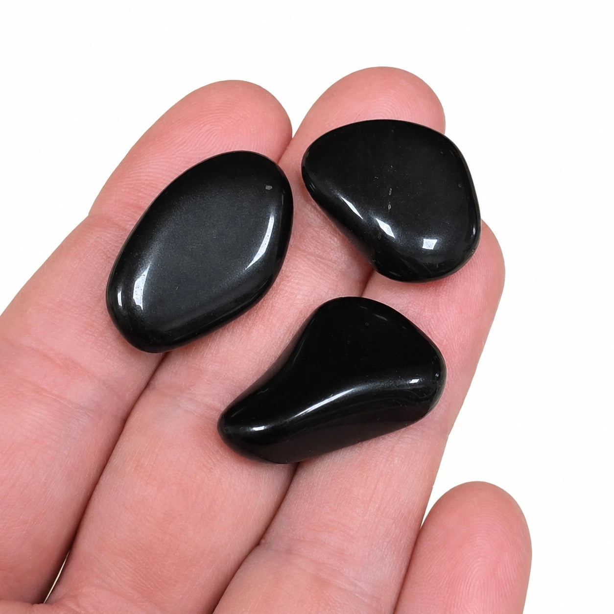 Trois pierres naturelles obsidienne noire roulée du Mexique présentées dans une main pour illustrer leur taille réelle de 2 à 3 cm, galets polis noirs destinés à la collection et à la lithothérapie.