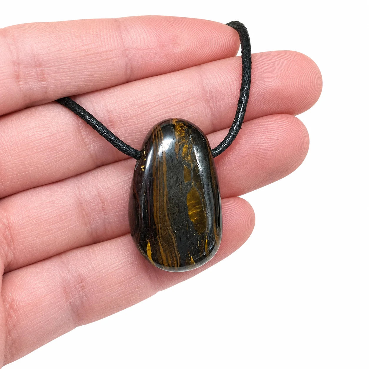 Pendentif œil de fer d'Australie en pierre percée naturelle présenté dans la main, montrant sa taille réelle et ses reflets métalliques.