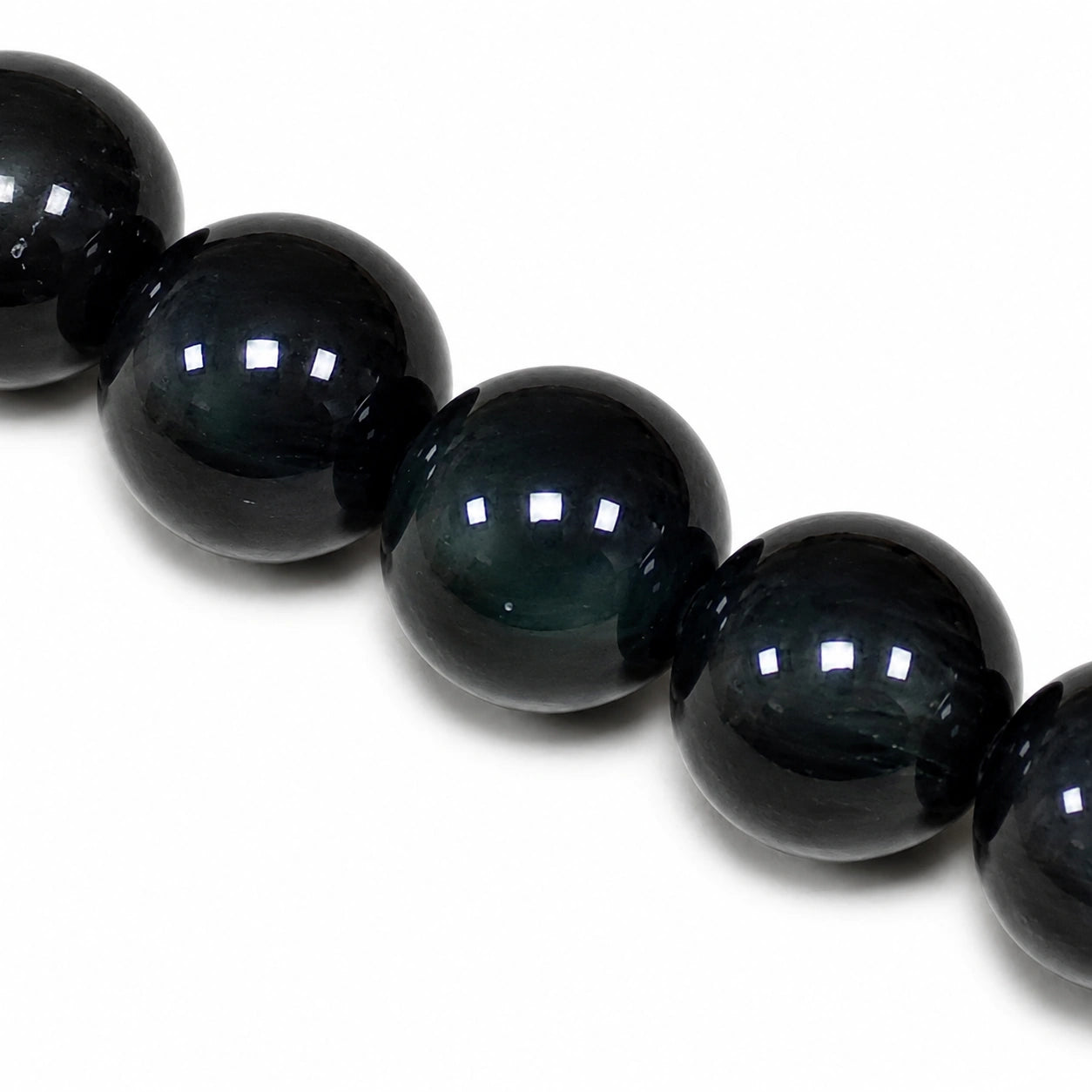 Macro des perles rondes de 8 mm d'un bracelet en obsidienne œil céleste véritable révélant les reflets irisés naturels de cette pierre volcanique noire.
