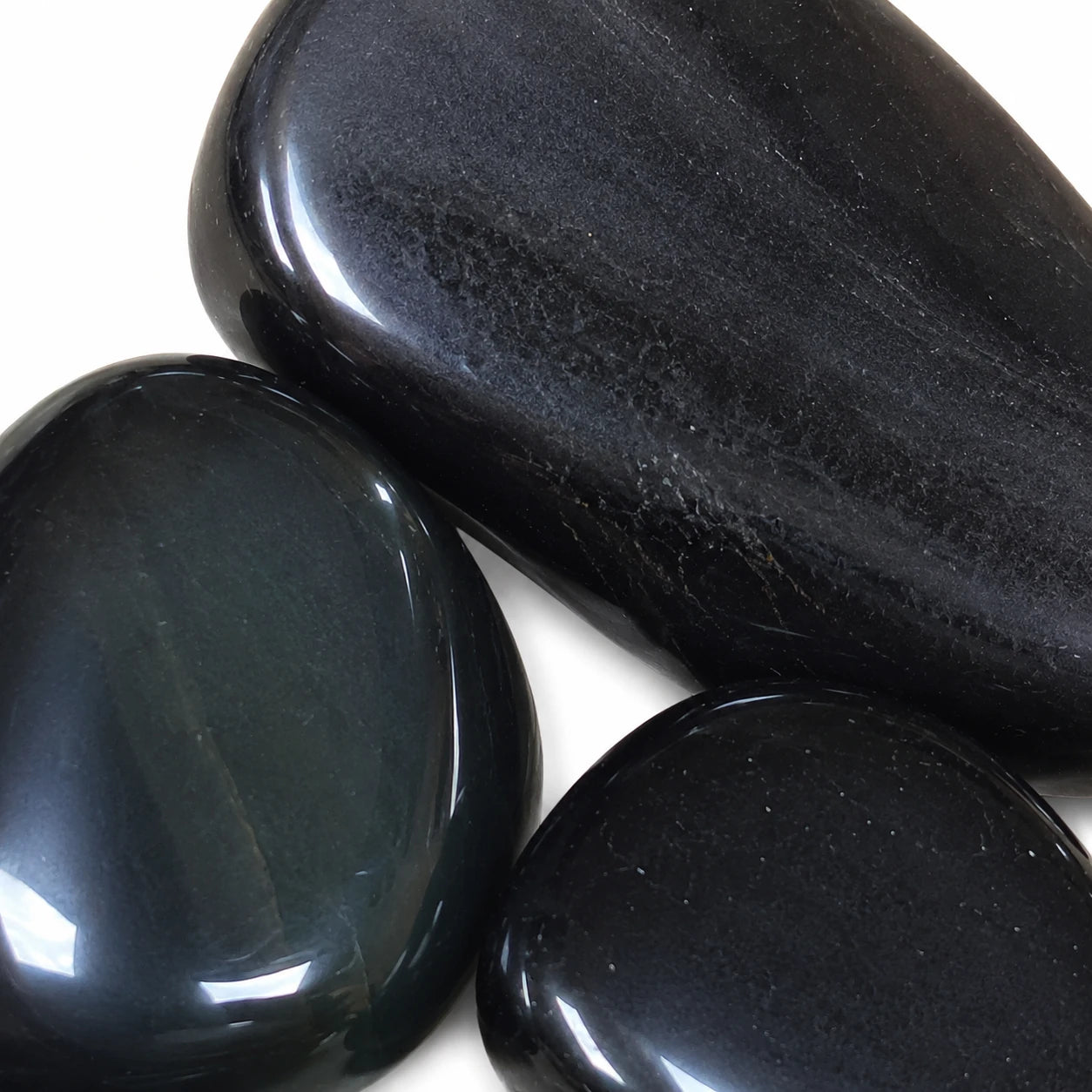 Gros plan sur trois pierres naturelles obsidienne œil céleste roulées du Mexique, mettant en valeur les reflets arc-en-ciel verts et gris caractéristiques de cette obsidienne volcanique polie.