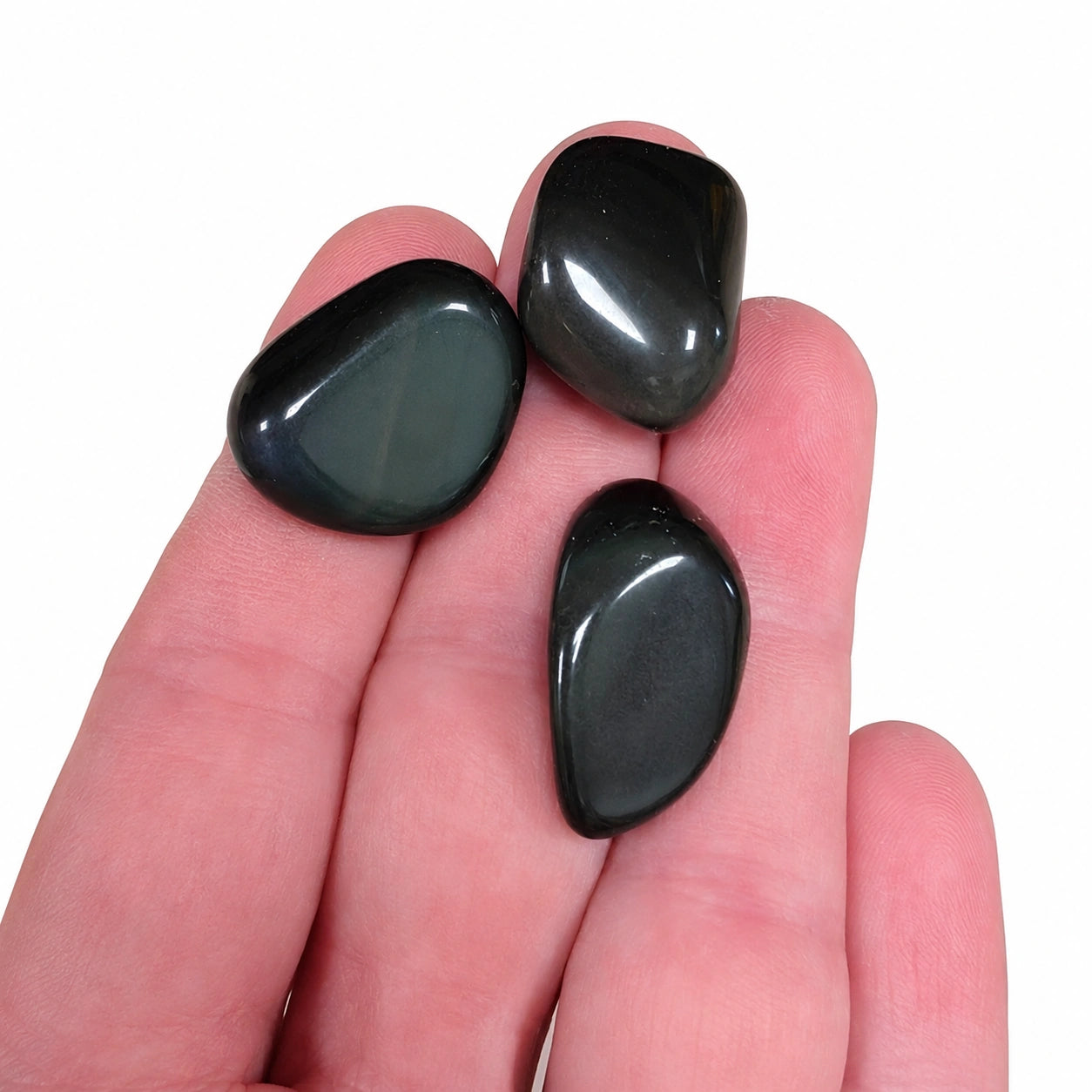 Trois pierres naturelles obsidienne œil céleste roulées du Mexique présentées dans une main pour montrer leur taille réelle de 2 à 3 cm, avec leurs reflets irisés naturels et leur finition polie.