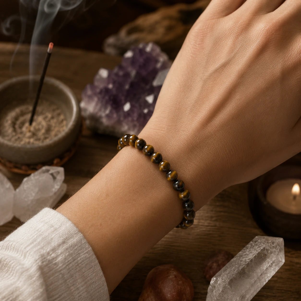 Bracelet Œil de tigre en perles rondes naturelles de 6 mm porté au poignet, dans une ambiance zen avec encens et minéraux, illustrant un bijou de lithothérapie élégant aux reflets dorés authentiques.