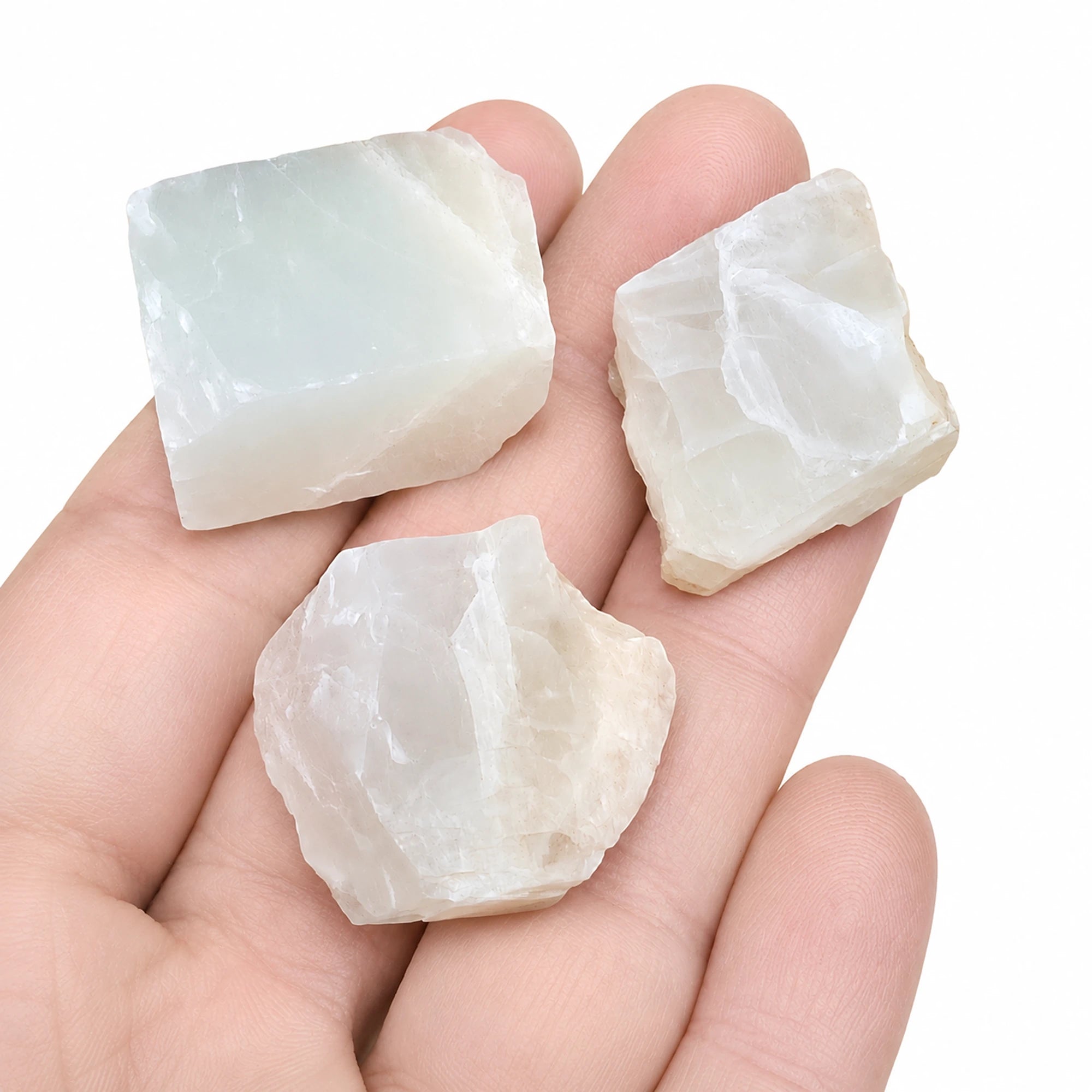 Trois pierres de lune brutes d'Inde présentées dans une main pour illustrer leur taille réelle de 2 à 3 cm, cristaux naturels blancs aux reflets nacrés.