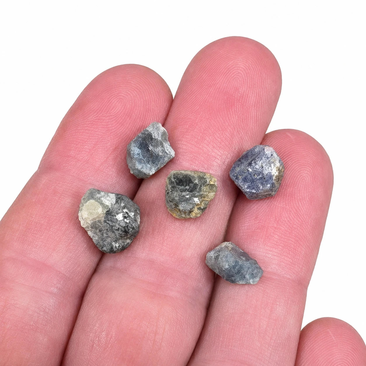 Petites pierres brutes de saphir bleu de Madagascar présentées dans une main pour montrer leur taille réelle de 1 à 2 cm, cristaux naturels non polis destinés à la collection ou à la lithothérapie.