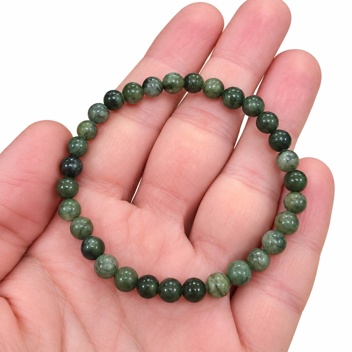 Bracelet en serpentine verte tenu dans une main, avec perles rondes polies de 6 mm aux nuances claires et foncées.