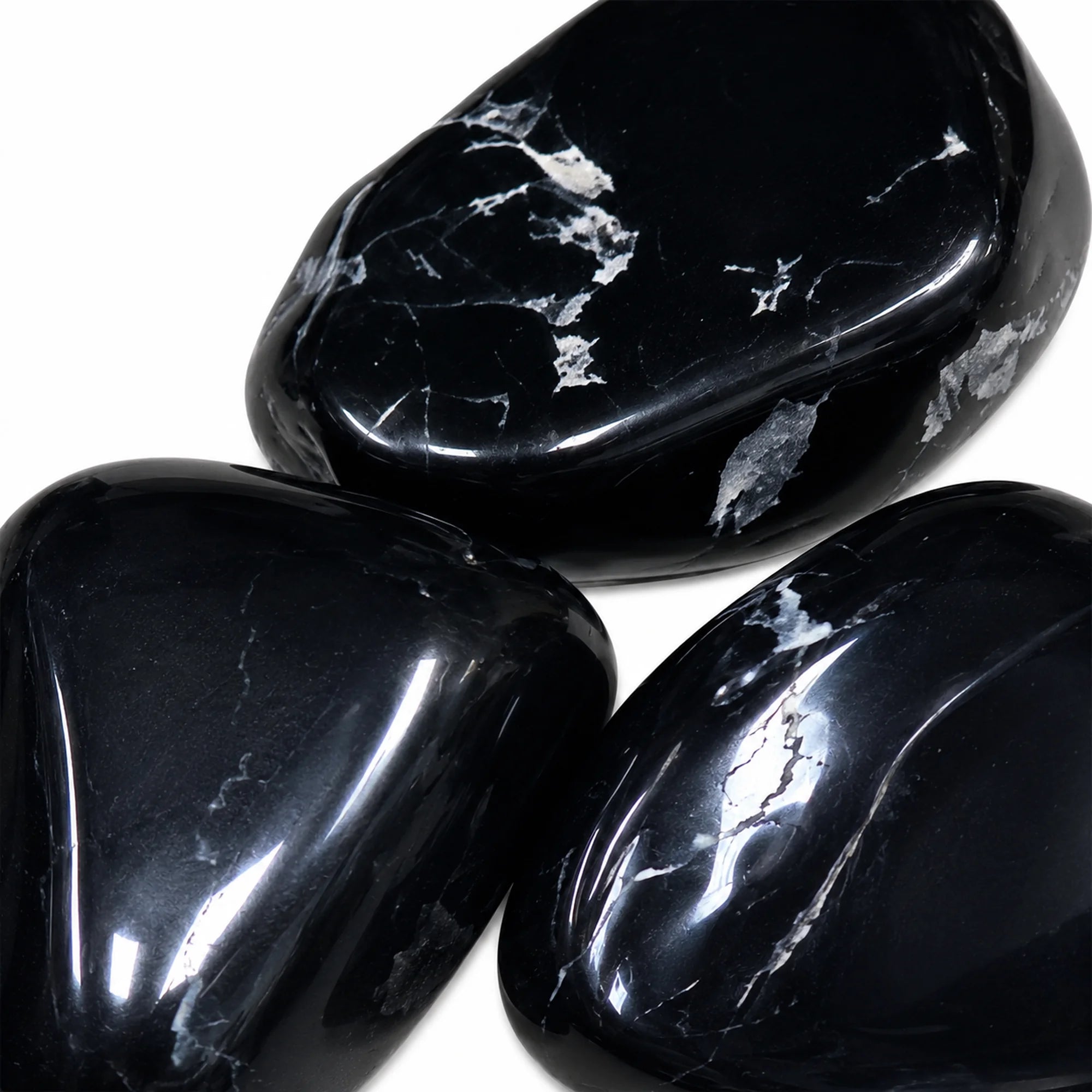 Gros plan sur trois pierres naturelles spinelle noir roulées de Chine, galets polis noirs montrant leur éclat vitreux et leurs veines minérales naturelles, photographiés sur fond blanc.