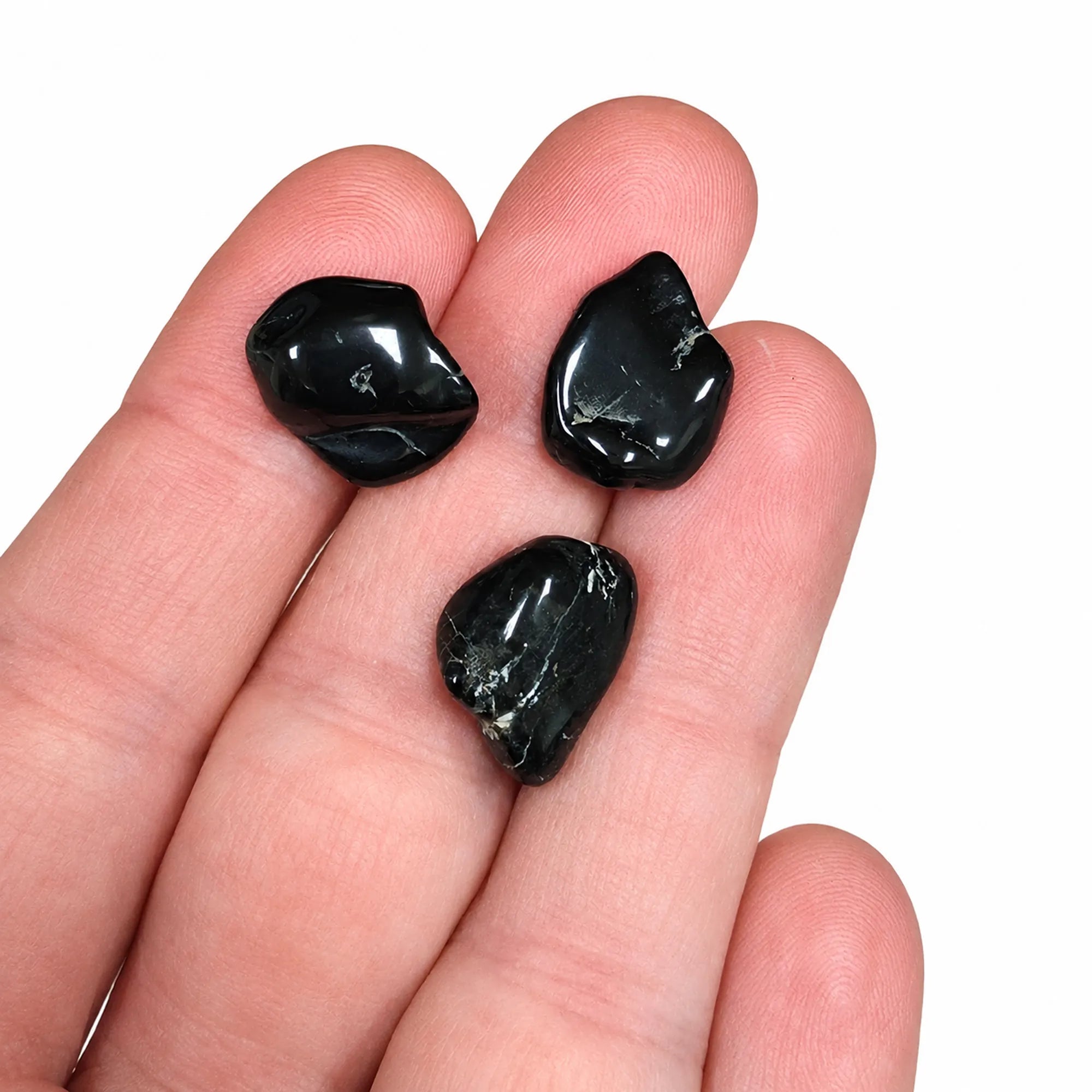Trois pierres naturelles spinelle noir roulées de Chine présentées dans une main pour illustrer leur taille réelle d'environ 1 à 2 cm, galets polis destinés à la lithothérapie et à la collection.