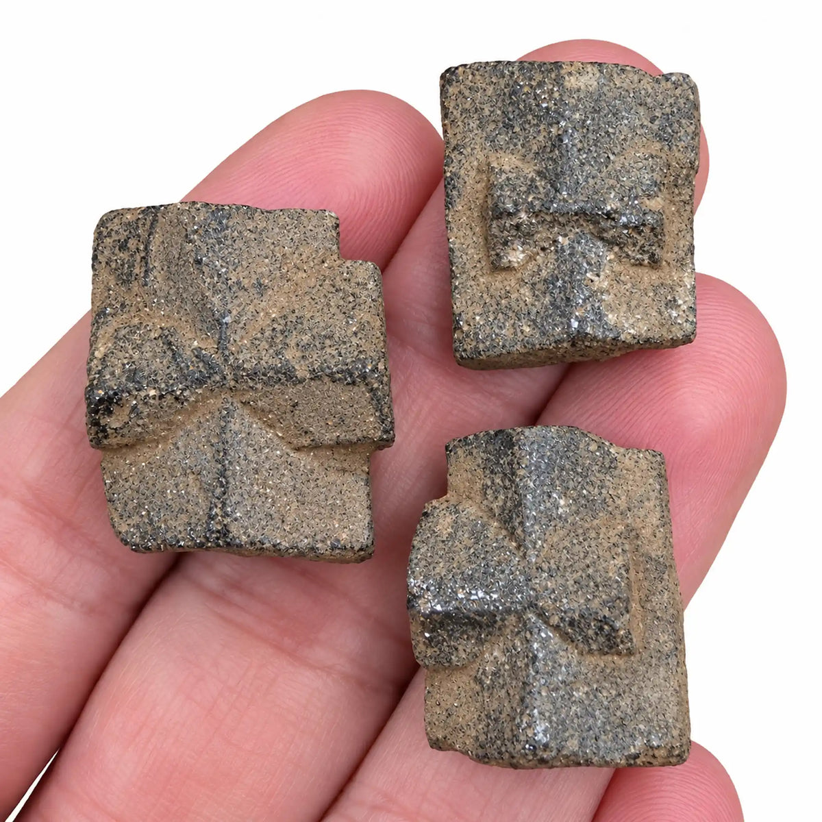 Trois pierres brutes staurotides de Bretagne, croix de Malte, présentées dans une main pour montrer leur taille, leur relief et leurs couleurs naturelles brun-gris.