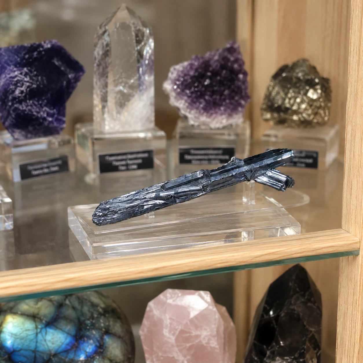 Stibine de Chine présentée sur un socle dans une vitrine de collection avec d'autres minéraux, cristal métallique naturel de 6 cm mis en valeur pour la vente.