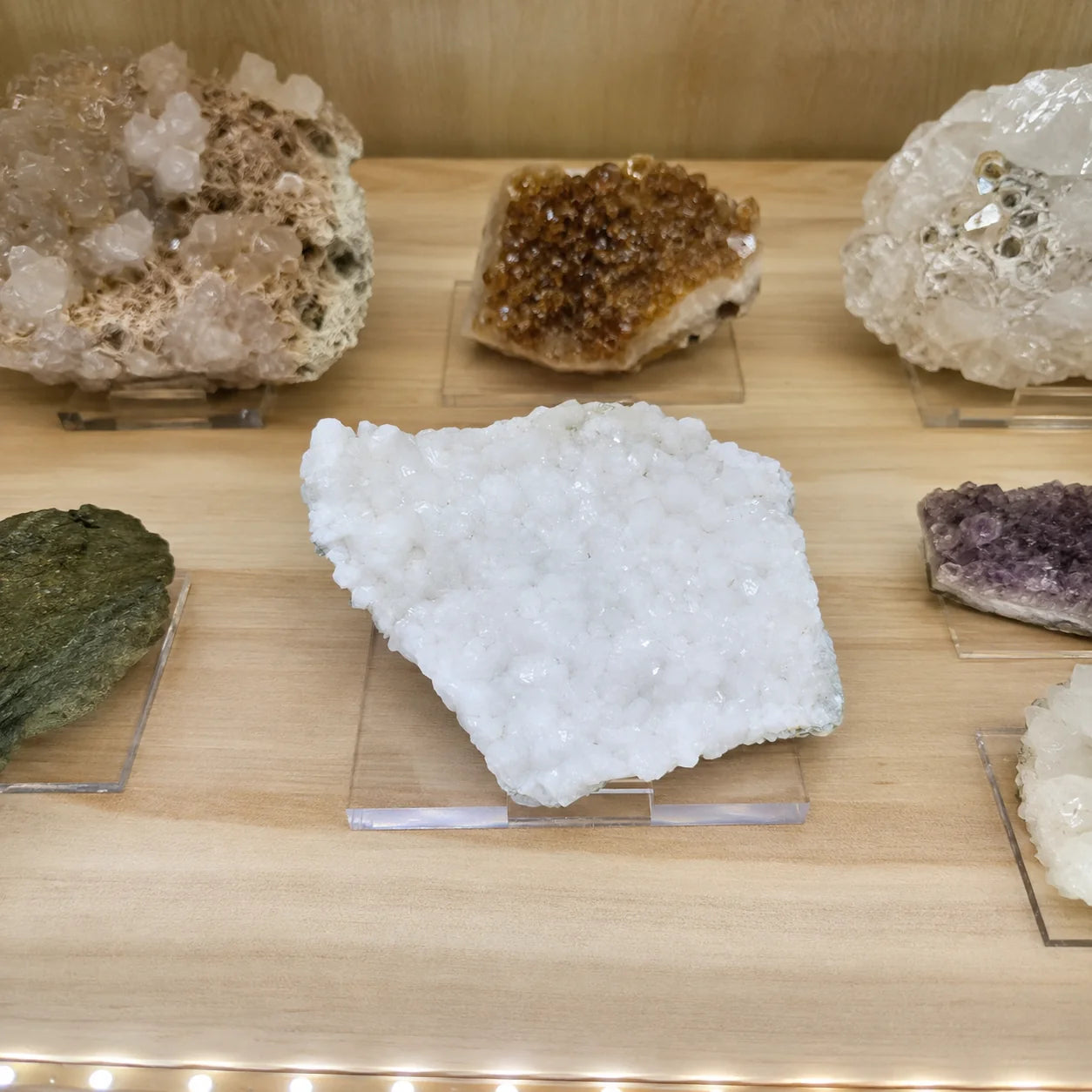 Druse de stilbite de 9 cm provenant du Hvalfjörður en Islande, présentée sur un socle dans une vitrine de minéraux afin d'illustrer sa taille réelle et son aspect de pièce de collection.