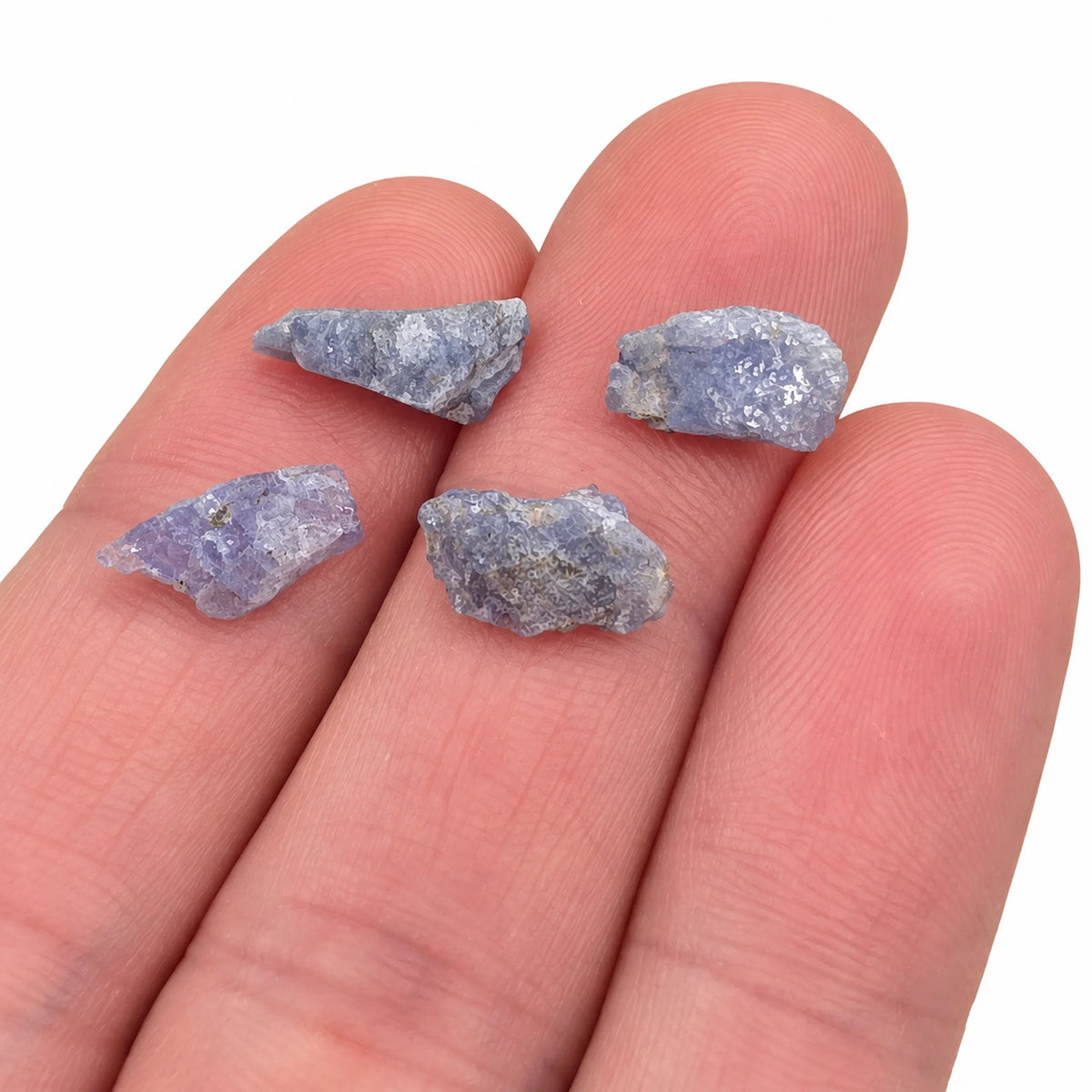 Pierres brutes de tanzanite chauffée de Tanzanie posées sur les doigts, petits cristaux naturels bleu violet