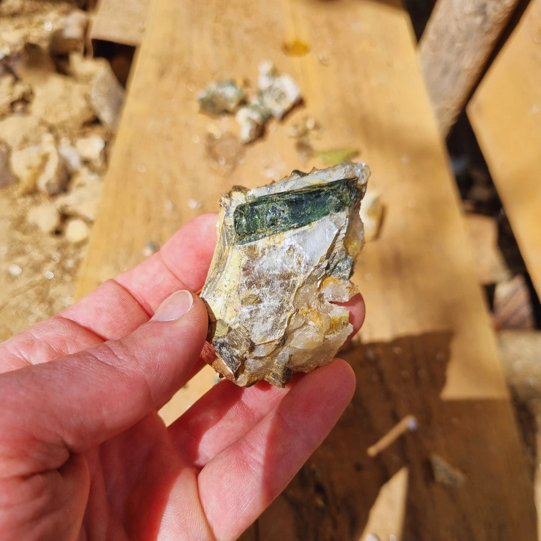 Cristal de tourmaline verte sur la roche tenu dans la main